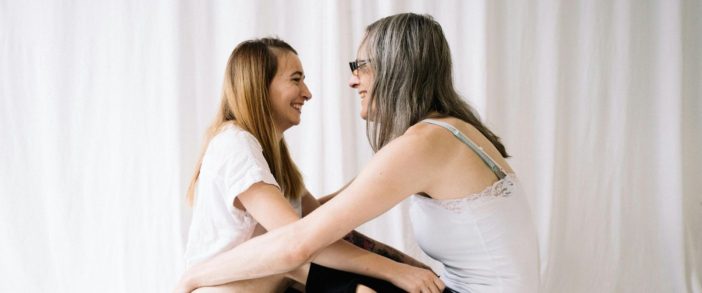 Two women facing one another on a bed, smiling.
